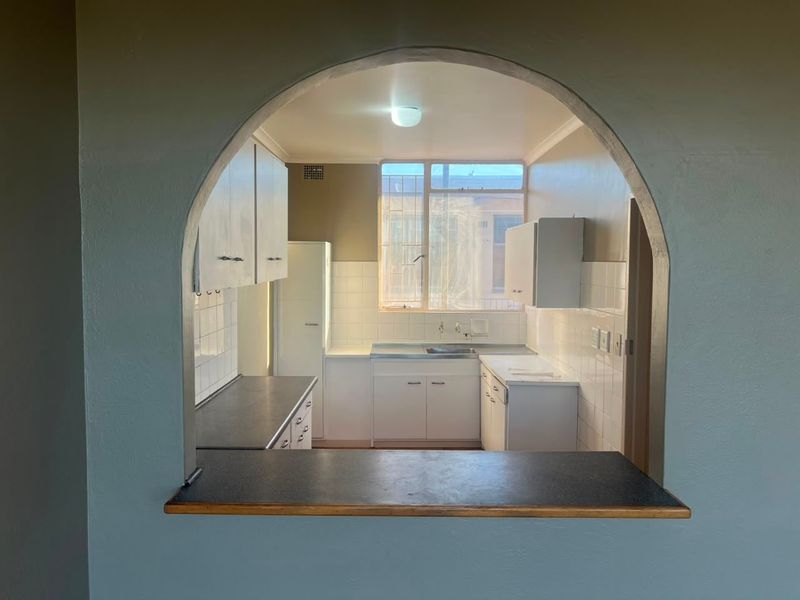 A functional kitchen featuring white cabinetry, laminate countertops, and a tiled backsplash, viewed through a classic architectural archway.