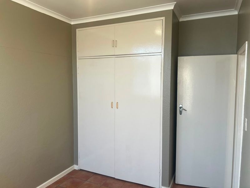 A clean, empty bedroom featuring a built-in wardrobe with overhead storage, tiled flooring, and neutral wall paint.