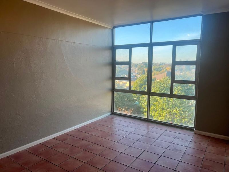 An empty bedroom featuring large aluminium-framed windows with natural light and tiled flooring, offering a clear view of the surrounding neighbourhood.