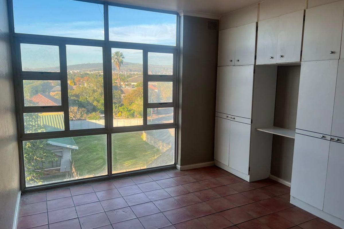 A bright, empty bedroom featuring large windows with scenic views, tiled flooring, and ample built-in cupboard storage.