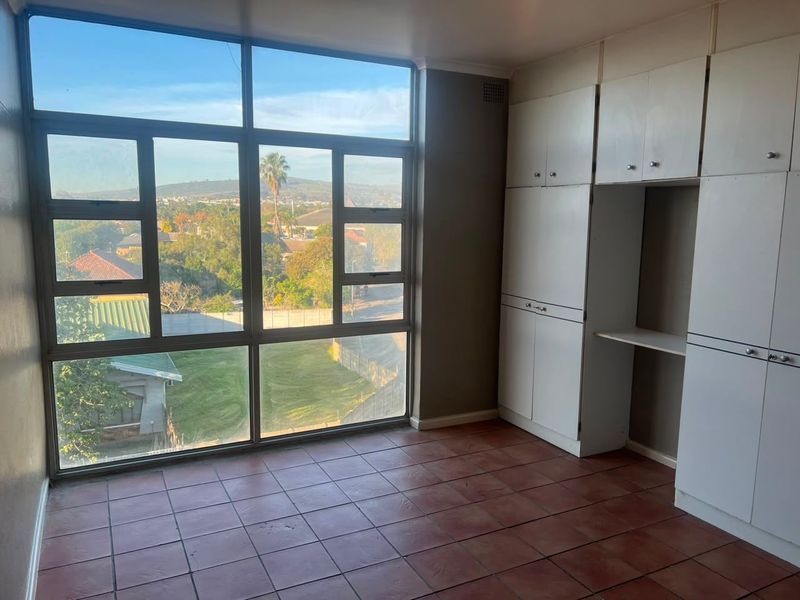 A bright, empty bedroom featuring large windows with scenic views, tiled flooring, and ample built-in cupboard storage.