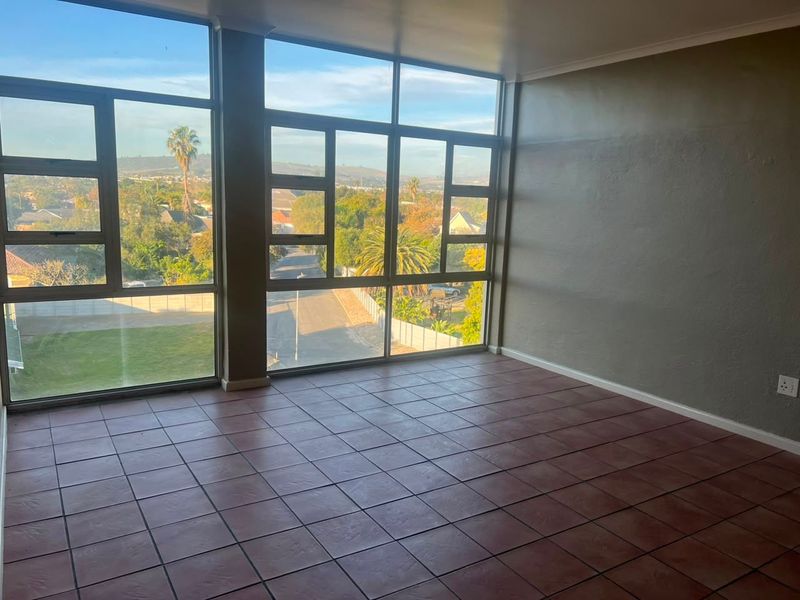 An empty living room featuring large floor-to-ceiling windows with expansive neighbourhood views and durable tiled flooring.
