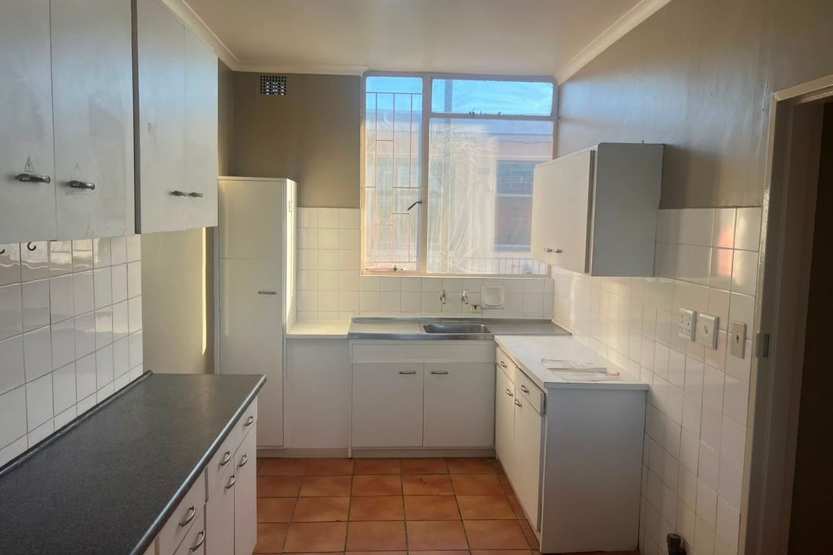 A functional, empty kitchen featuring white built-in cabinetry, tiled splashbacks, and tiled flooring, offering a blank canvas for modern renovation.