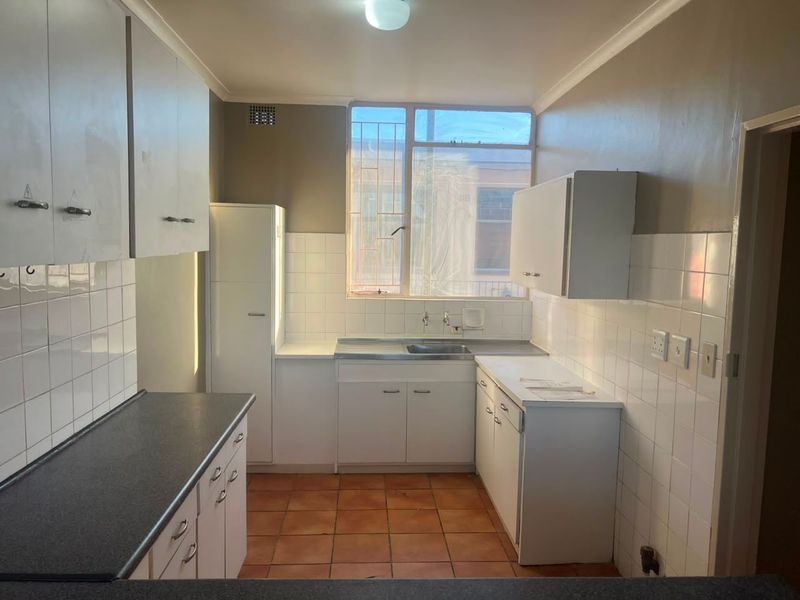 A functional, empty kitchen featuring white built-in cabinetry, tiled splashbacks, and tiled flooring, offering a blank canvas for modern renovation.