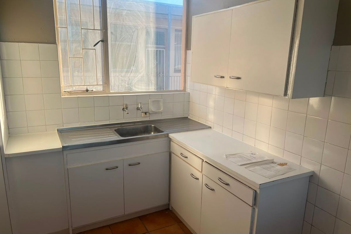 A compact, dated kitchen featuring white built-in cabinetry, a stainless steel sink, and tiled splashbacks, ready for a modern renovation.