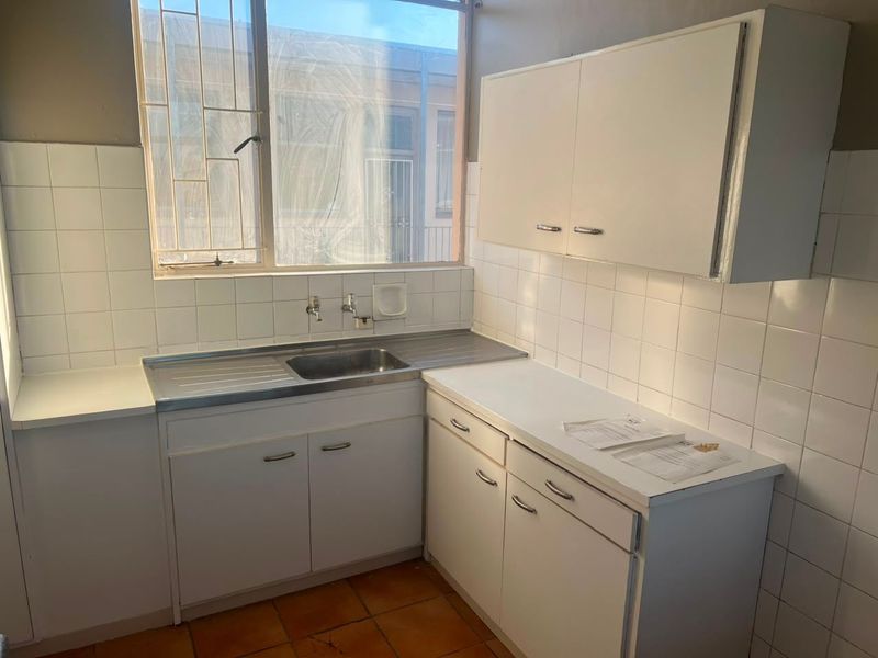 A compact, dated kitchen featuring white built-in cabinetry, a stainless steel sink, and tiled splashbacks, ready for a modern renovation.
