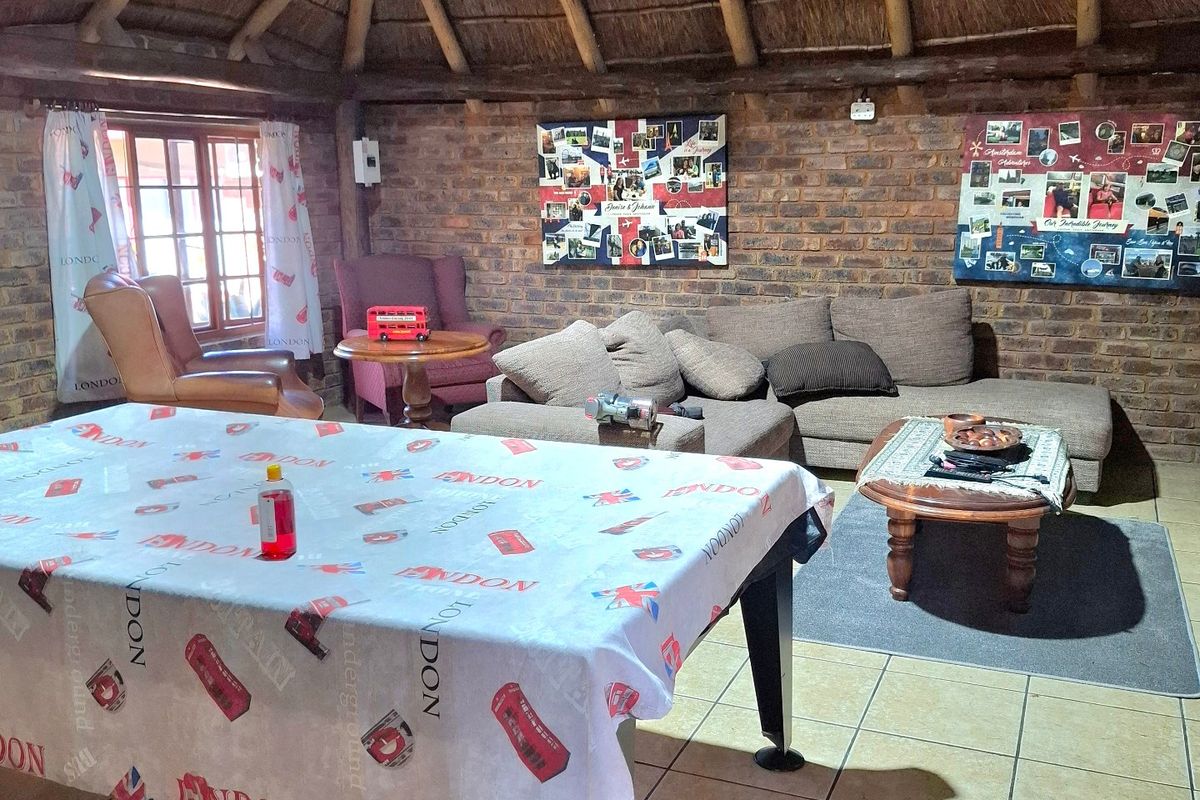 Spacious living area featuring a traditional thatched roof with exposed timber rafters, rustic exposed brick walls, and durable tiled flooring.