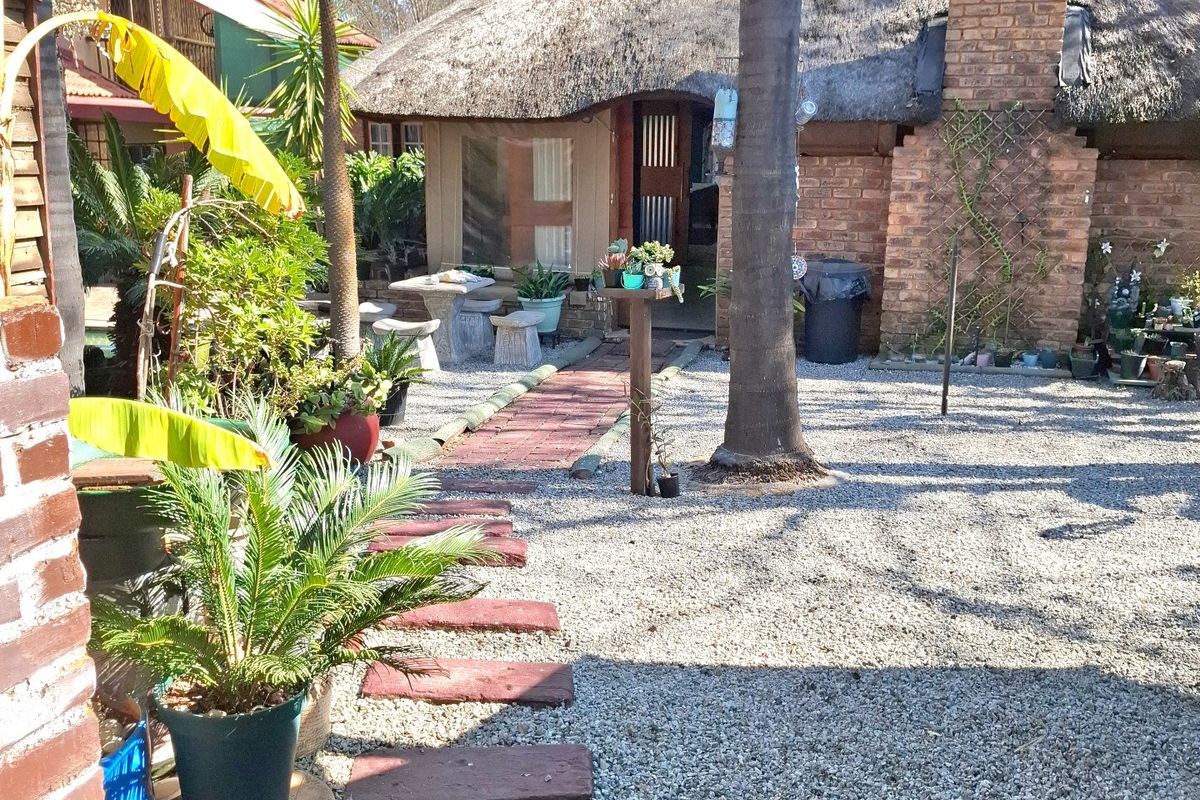A rear garden view featuring a traditional thatched roof house with brick chimney, stone pathways, and gravel landscaping.