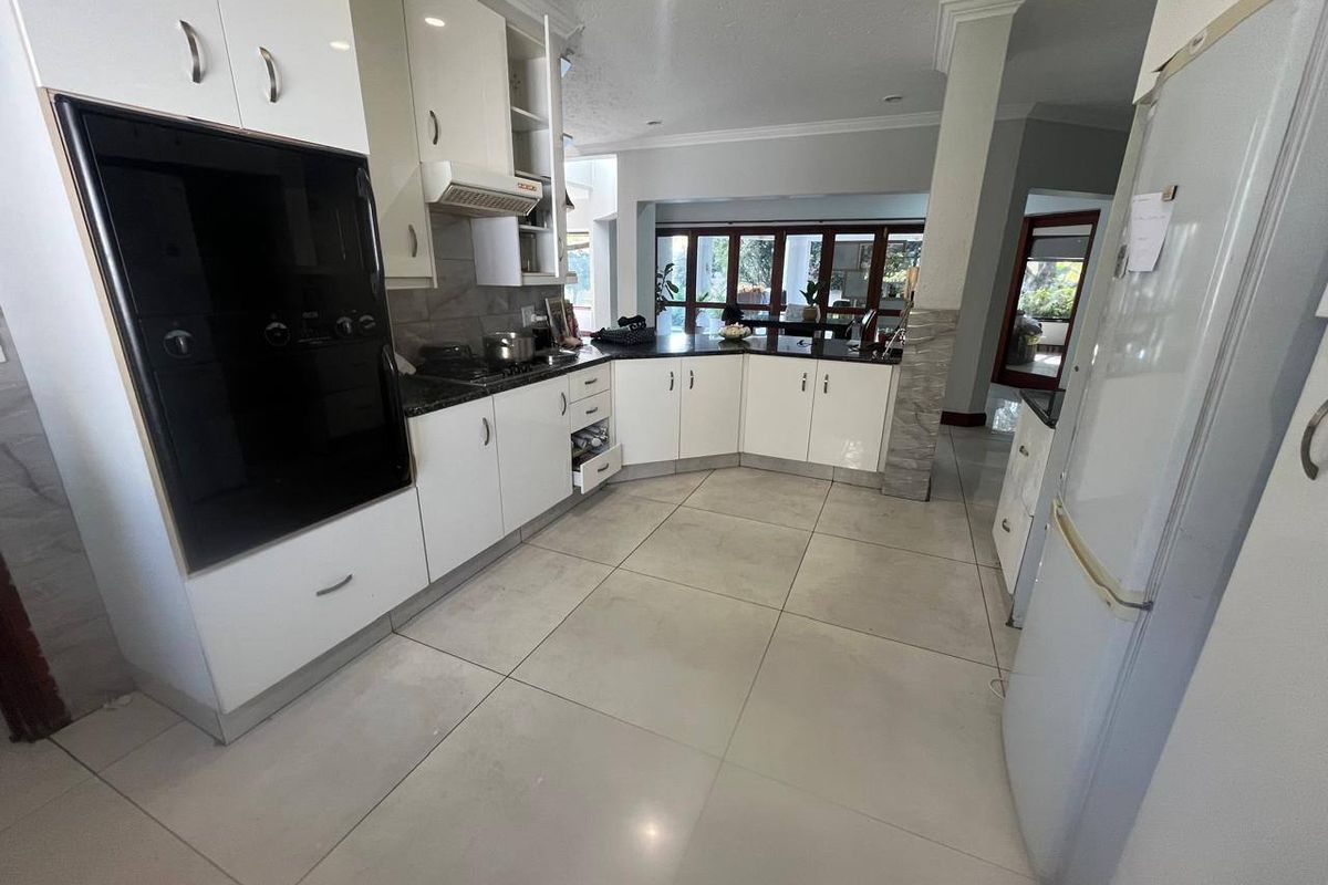 A functional kitchen featuring white cabinetry, dark granite countertops, built-in oven, and large format floor tiles, opening into an adjacent living area.