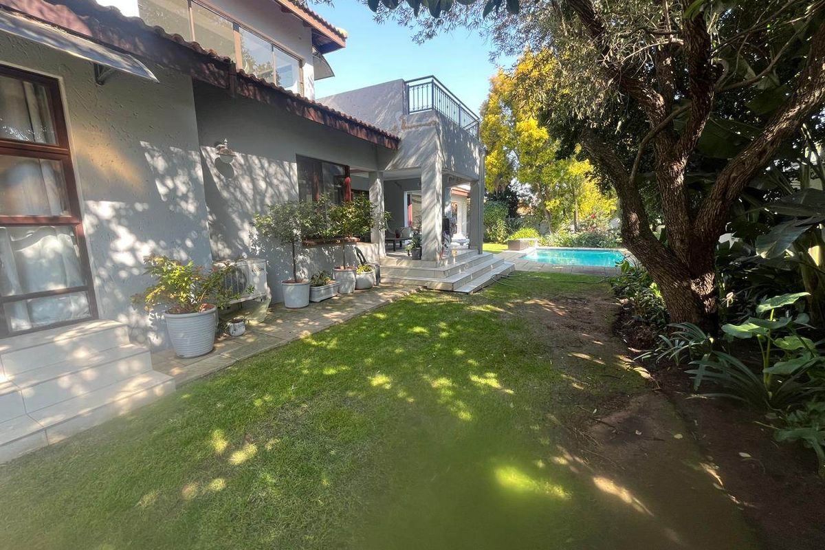 Rear view of the property featuring a landscaped garden, tiled patio area, balcony, and a swimming pool.