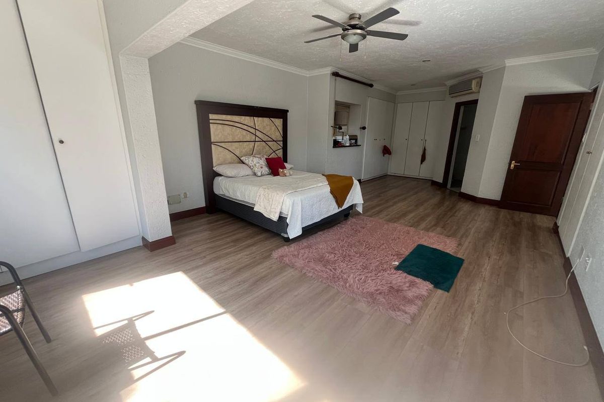 Spacious bedroom featuring laminate flooring, built-in cupboards, a ceiling fan, and an integrated air conditioning unit.