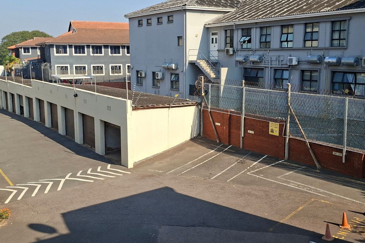 Exterior view of the apartment complex featuring a garage block, paved parking area, and secure perimeter fencing.