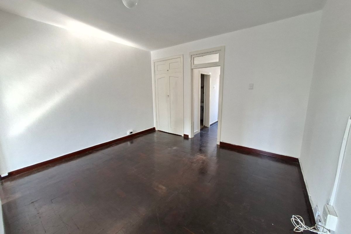 An empty bedroom featuring dark parquet flooring, a built-in cupboard, and a doorway with a transom window leading to an adjacent space.