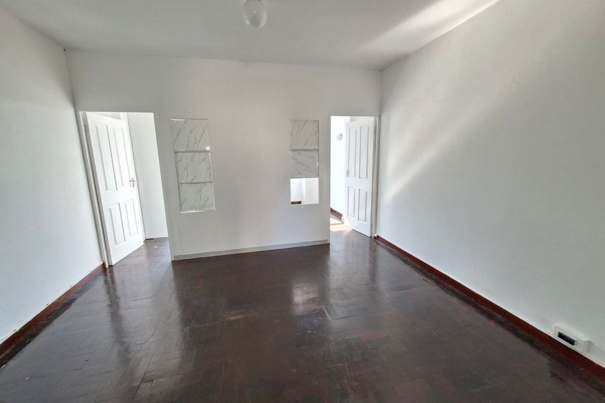 An empty living room featuring dark parquet flooring, white walls, and two internal doorways with decorative wall cutouts.