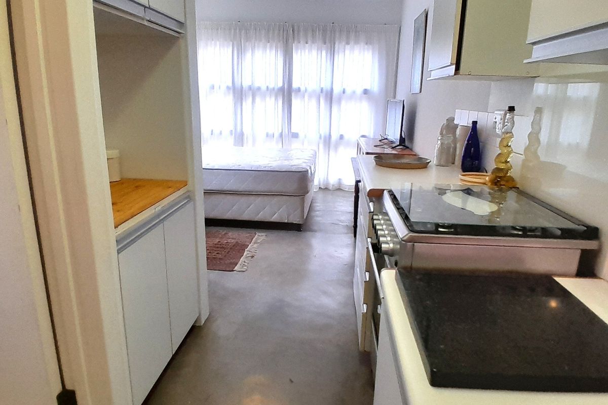 Open plan kitchen and living area featuring built-in cabinetry, gas stove, and concrete flooring, leading to a bright bedroom space.
