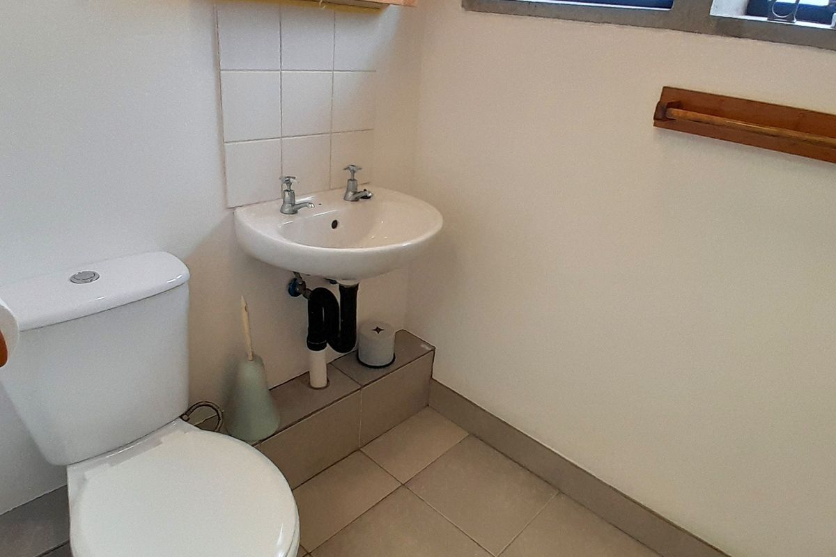 A functional bathroom featuring a wall-mounted basin, ceramic toilet, tiled flooring, and a wooden framed mirror, providing a clean and practical space.