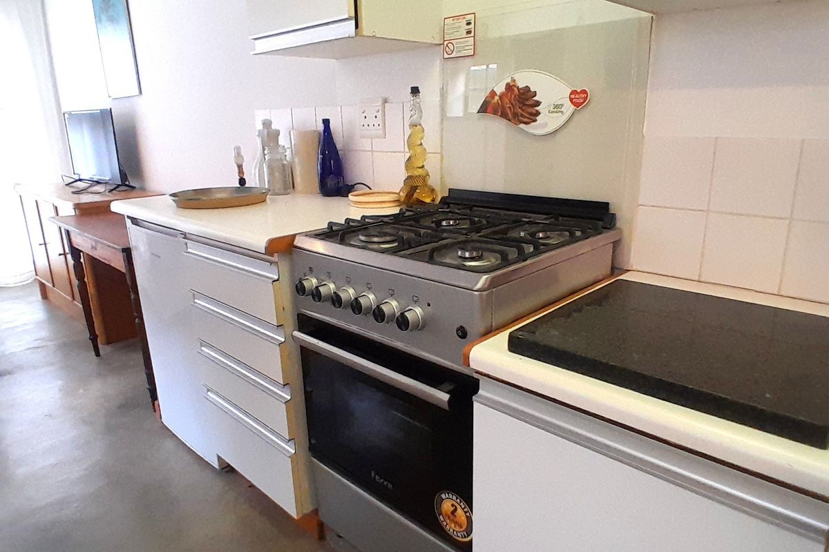 A compact kitchen area featuring a gas stove, oven, extractor fan, and tiled backsplash, showing signs of wear on the cabinetry.