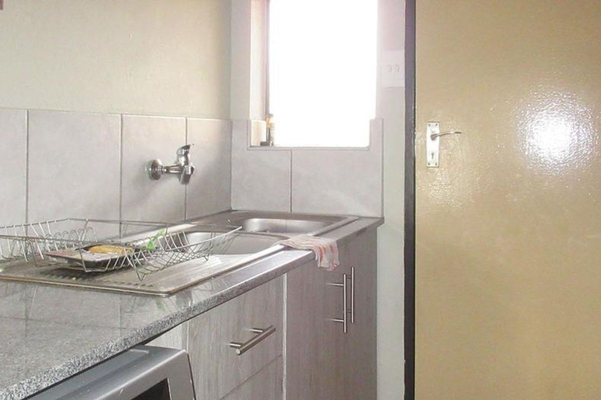 A functional kitchen area featuring granite countertops, a stainless steel sink, tiled backsplash, and built-in cabinetry.