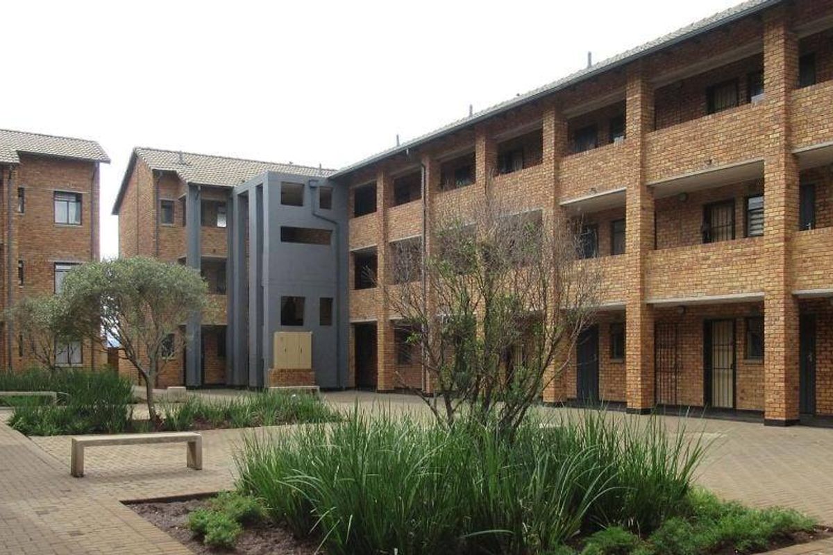 A view of the apartment complex courtyard featuring face brick architecture, paved walkways, landscaped garden beds, and multi-level balcony access.