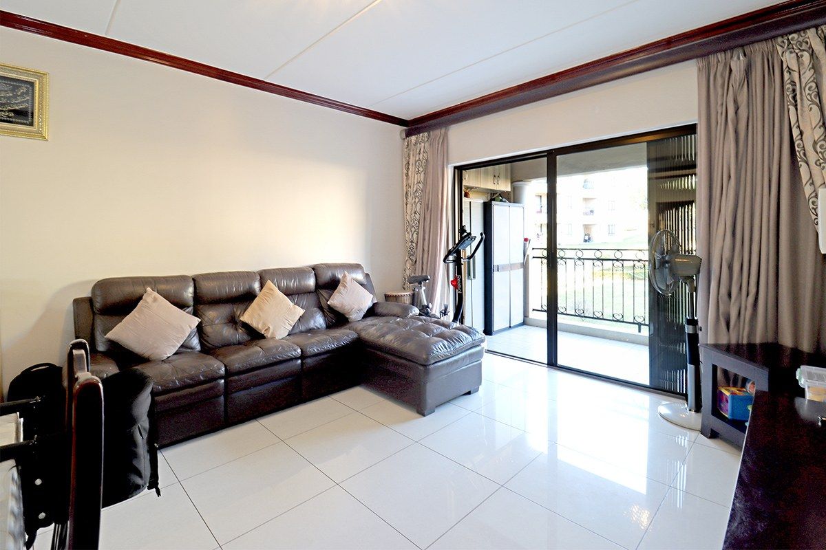 Spacious living room featuring polished white floor tiles, crown molding, and large sliding glass doors providing access to a private balcony.