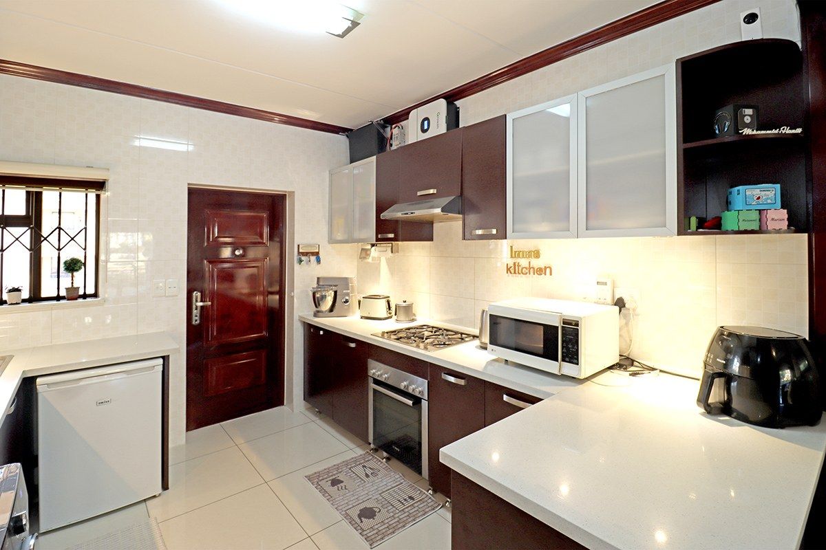 A well-maintained kitchen featuring dark wood cabinetry, quartz countertops, a gas hob, built-in oven, and tiled finishes throughout.