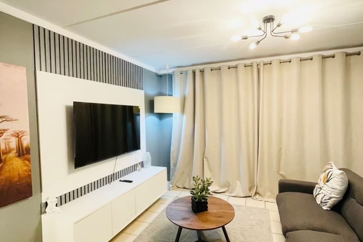 A well-maintained living room featuring a modern built-in media console, decorative wall paneling, and neutral tiled flooring.