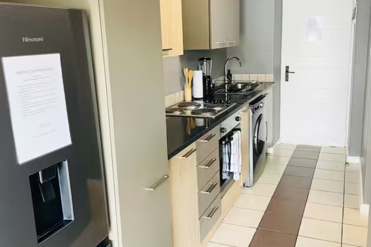 A compact, functional kitchen featuring modern light wood cabinetry, black granite countertops, integrated appliances, and a clean tiled floor.