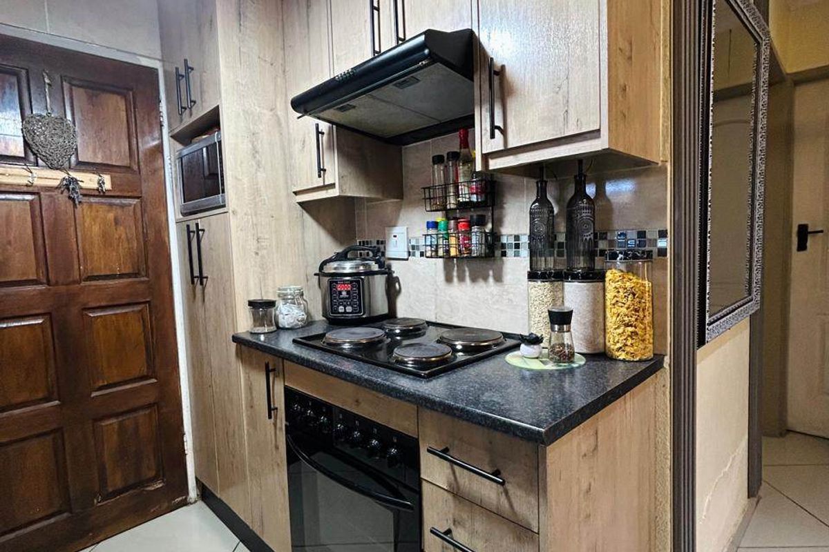 Compact kitchen featuring wood-look cabinetry, dark countertops, built-in oven, electric hob, extractor fan, and tiled flooring.