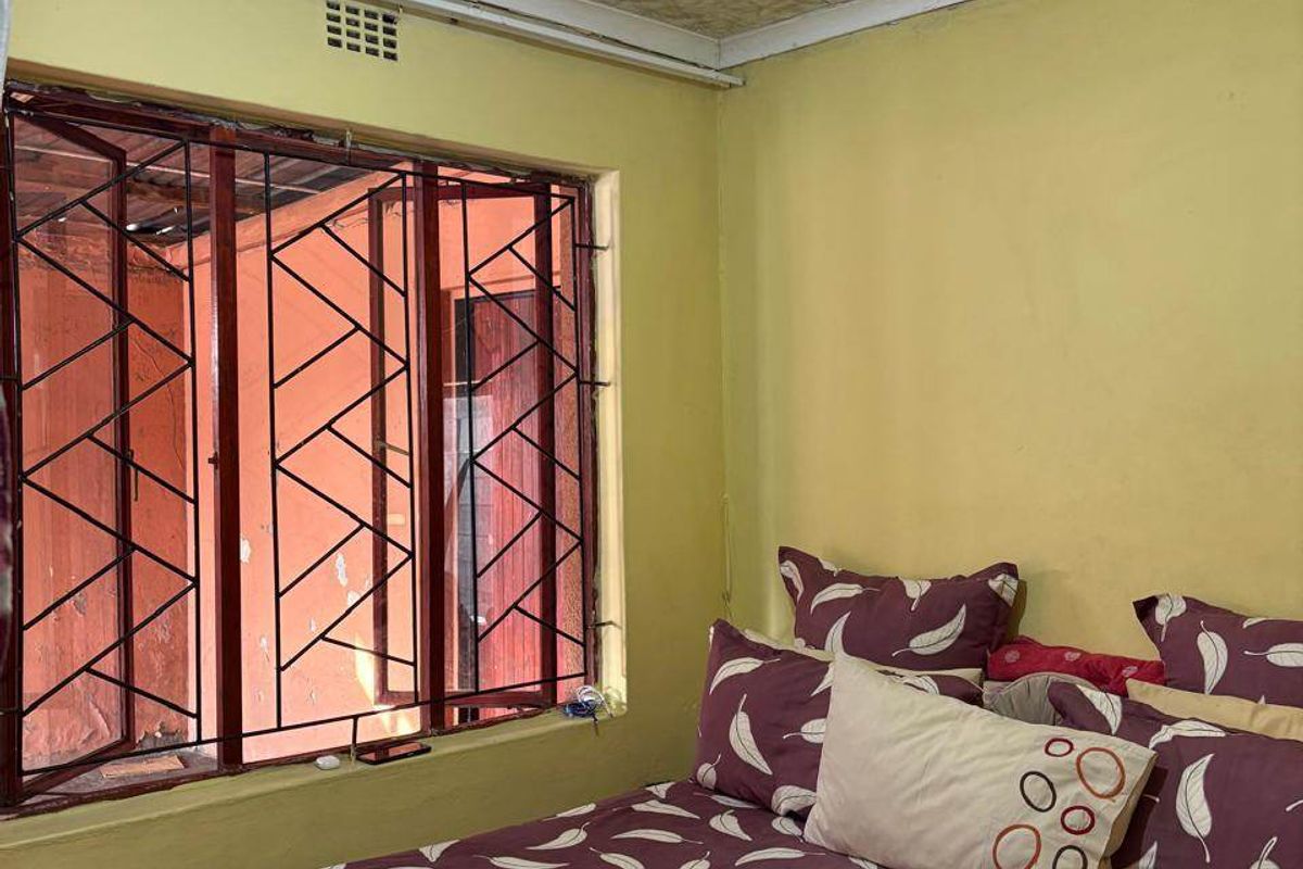 A bedroom featuring textured ceiling tiles, security bars on the window, and a ventilation grille, requiring cosmetic updates to improve the overall aesthetic.