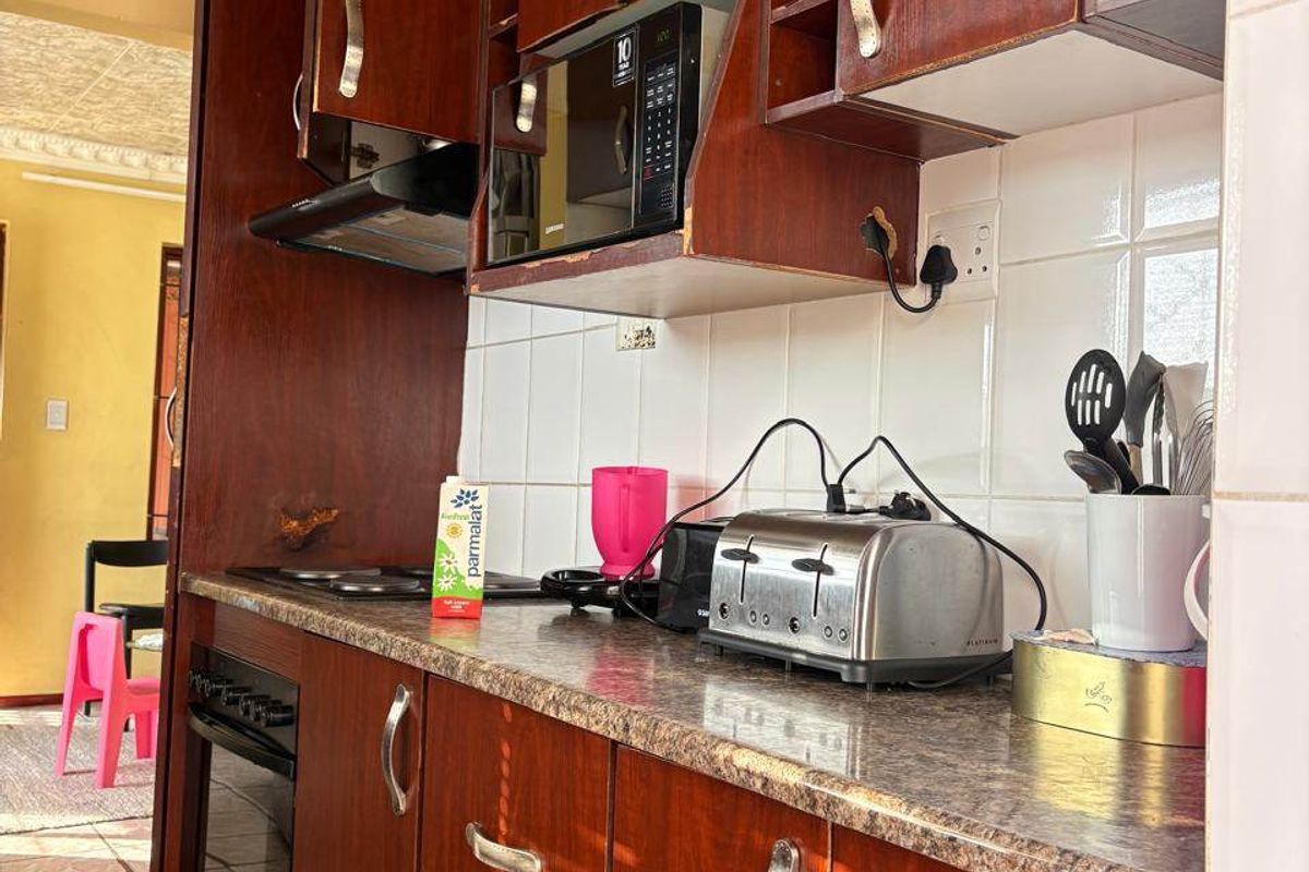 A functional kitchen featuring dark wood-toned cabinetry, laminate countertops, built-in oven, hob, and extractor fan with a tiled backsplash.