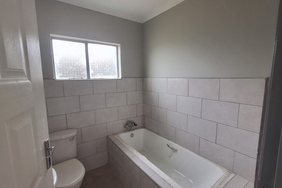 A functional bathroom featuring a built-in bathtub, toilet, and neutral wall tiling, offering a blank canvas for potential cosmetic updates.