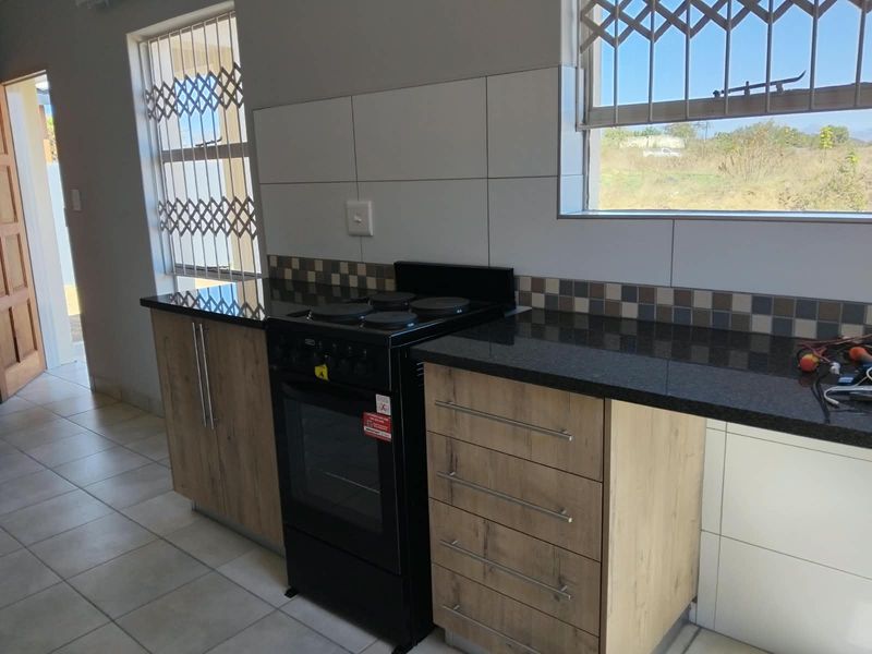 Modern kitchen featuring wood-finish cabinetry, granite countertops, a freestanding stove, and tiled splashbacks with security-fitted windows.
