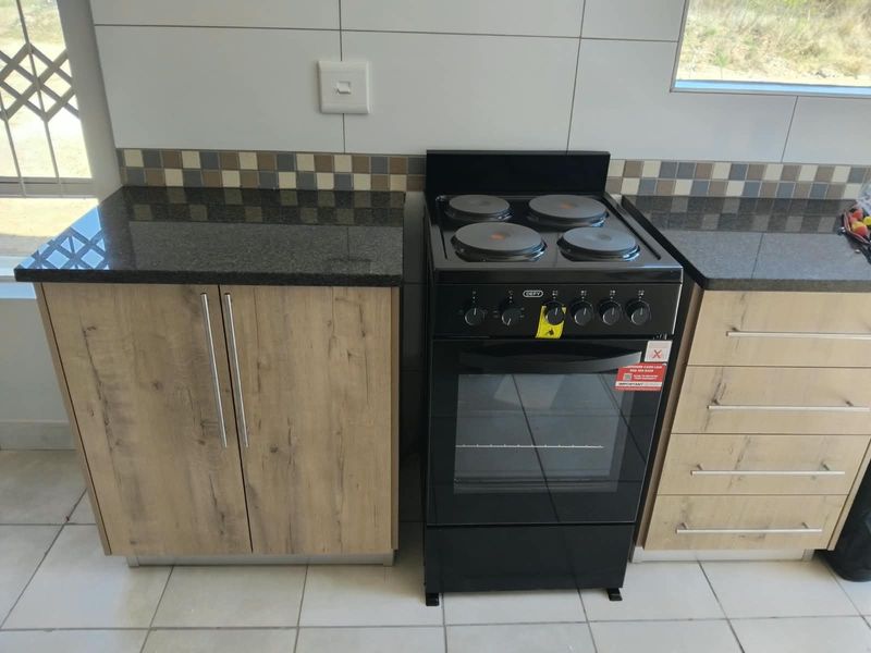 Modern kitchen area featuring wood-finish cabinetry, dark granite countertops, a tiled backsplash, and a freestanding electric stove.