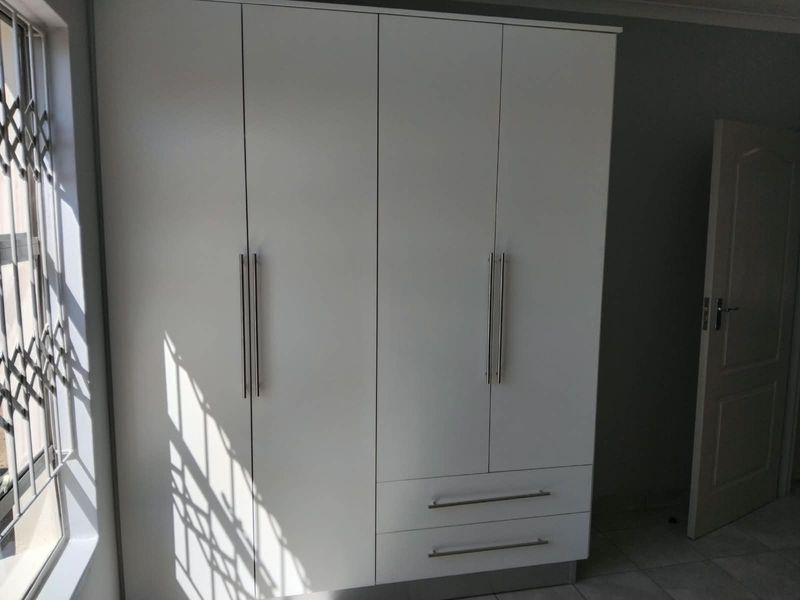 A clean bedroom featuring a modern white built-in wardrobe with sleek handles and a window fitted with a security gate.