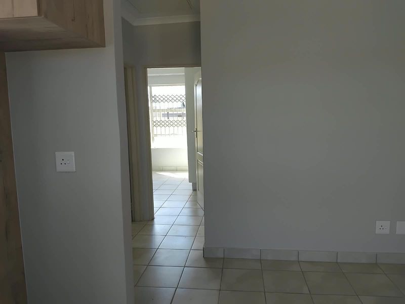 A neutral-toned hallway featuring tiled flooring and a security gate leading to an adjacent space, providing a clean and functional transition area.