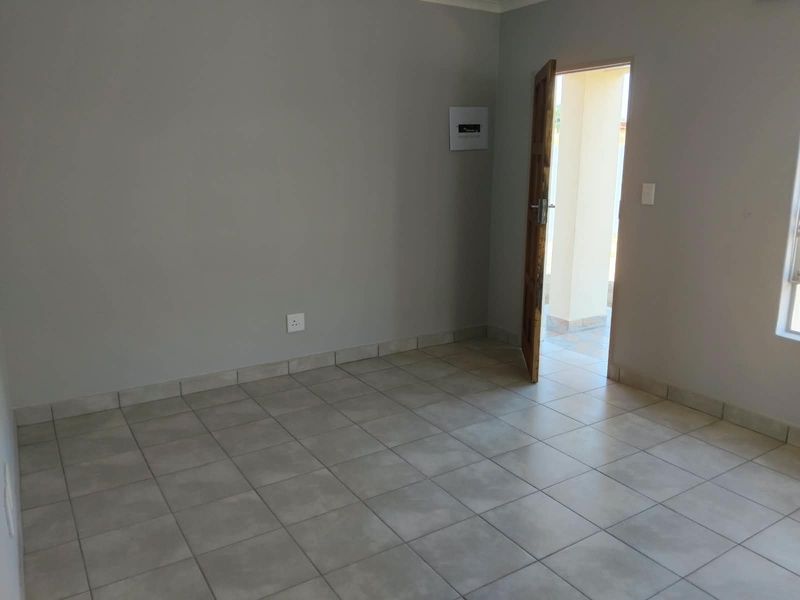 An empty, neutral-toned living area featuring tiled flooring, a wall-mounted electrical distribution board, and direct access to an outdoor patio space.