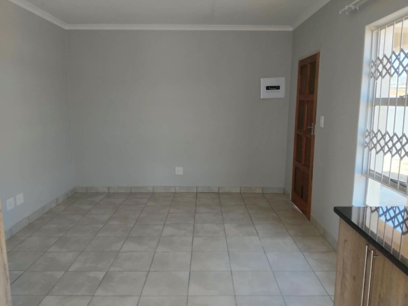 A clean, empty living area featuring neutral tiled flooring, a timber door with security gate, and a wall-mounted electrical distribution board.