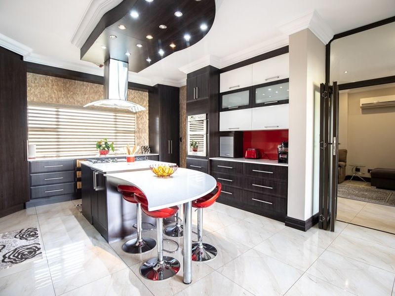 Modern kitchen featuring a central island with breakfast bar, high-gloss cabinetry, built-in appliances, and polished tiled flooring with recessed ceiling lighting.
