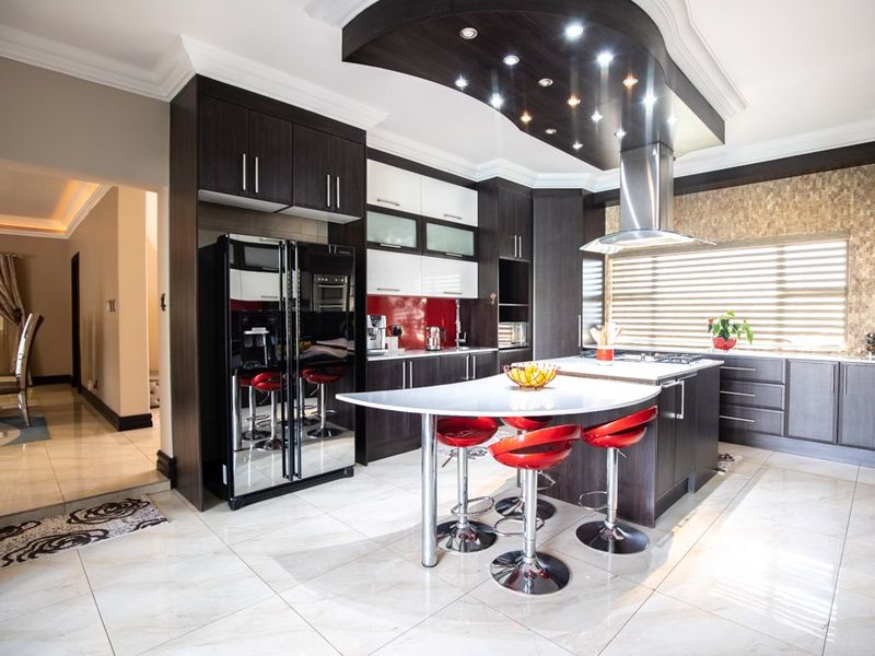 Modern kitchen featuring dark wood cabinetry, a central island with breakfast bar, stone countertops, and integrated lighting under a decorative bulkhead.