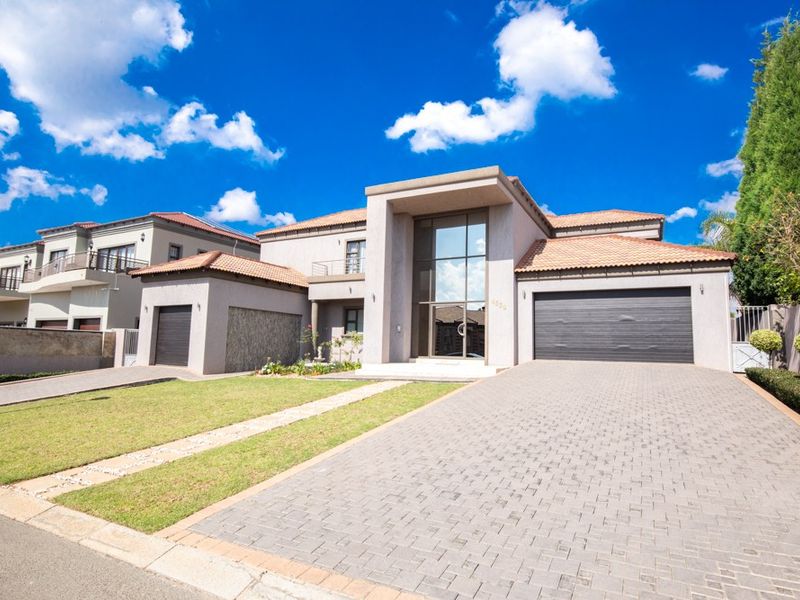 Modern double-storey residence featuring a double garage, paved driveway, and a striking double-volume glass entrance facade.