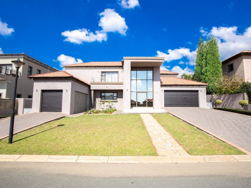 Modern double-story residence featuring a prominent glass entrance, dual garages, paved driveways, and a well-maintained front lawn.