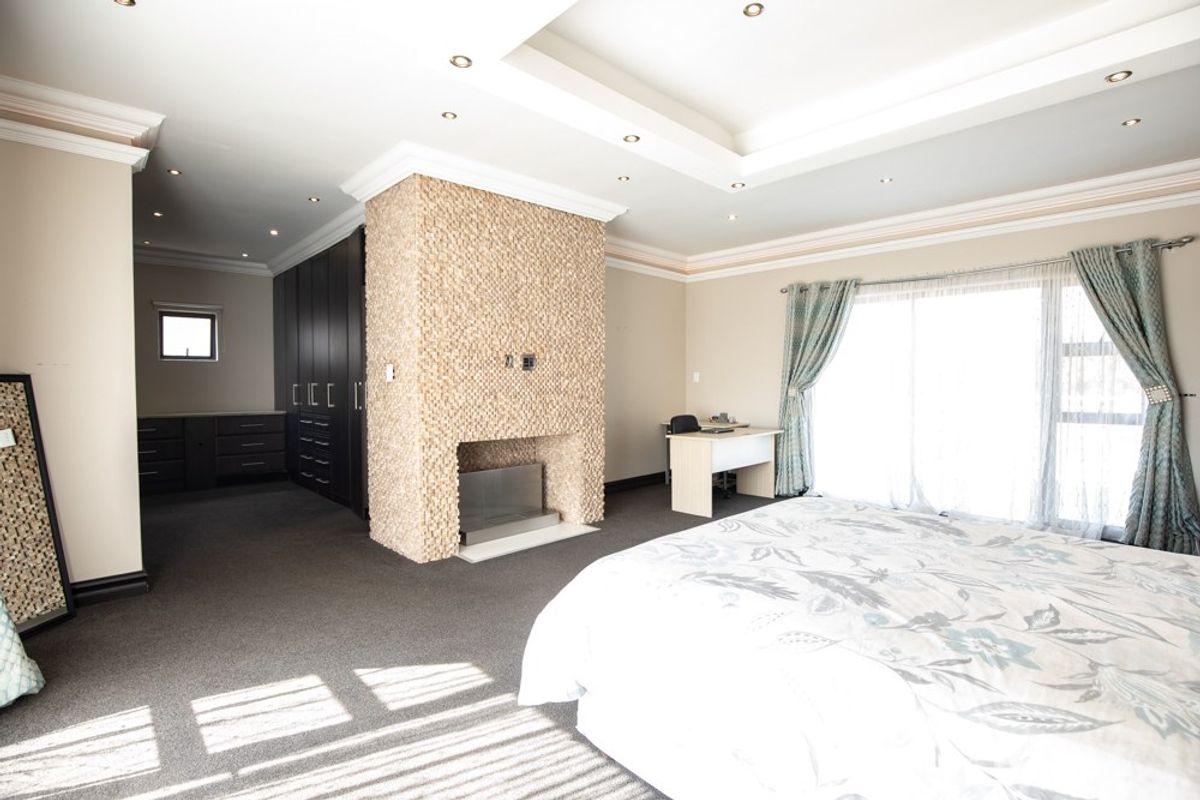 Spacious bedroom featuring a central stone-clad fireplace, built-in cabinetry, recessed ceiling with downlights, and large sliding doors providing ample natural light.