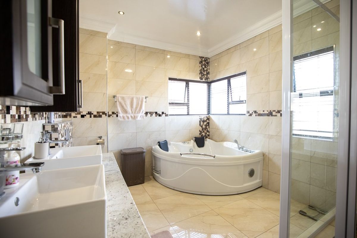 Modern bathroom featuring a corner spa bath, double vanity with granite countertop, glass shower enclosure, and neutral floor-to-ceiling tiling.