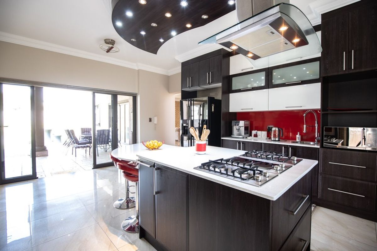 Modern kitchen featuring a central island with gas hob, dark wood cabinetry, stone countertops, and direct access to an outdoor patio area.
