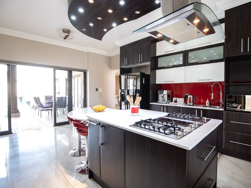 Modern kitchen featuring a central island with gas hob, dark wood cabinetry, stone countertops, and direct access to an outdoor patio area.