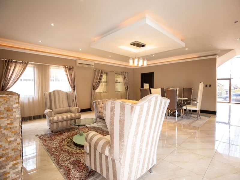 Spacious open-plan living and dining area featuring polished tiled floors, a decorative recessed ceiling with downlights, and a stone-clad feature pillar.