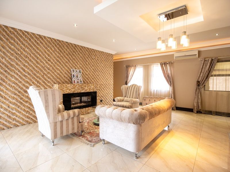 Spacious living room featuring a modern built-in fireplace, decorative tiled feature wall, recessed ceiling with downlights, and polished floor tiles.