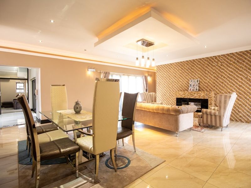Spacious open-plan living and dining area featuring a modern fireplace, decorative feature wall, recessed ceiling lighting, and polished floor tiles.