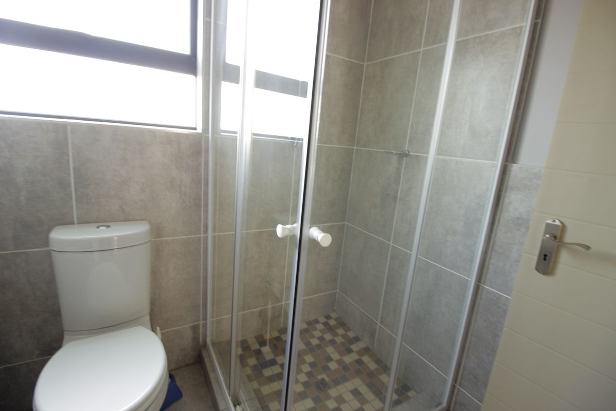 A clean, functional bathroom featuring a glass-enclosed shower, modern toilet, and neutral grey wall tiling with mosaic floor accents.