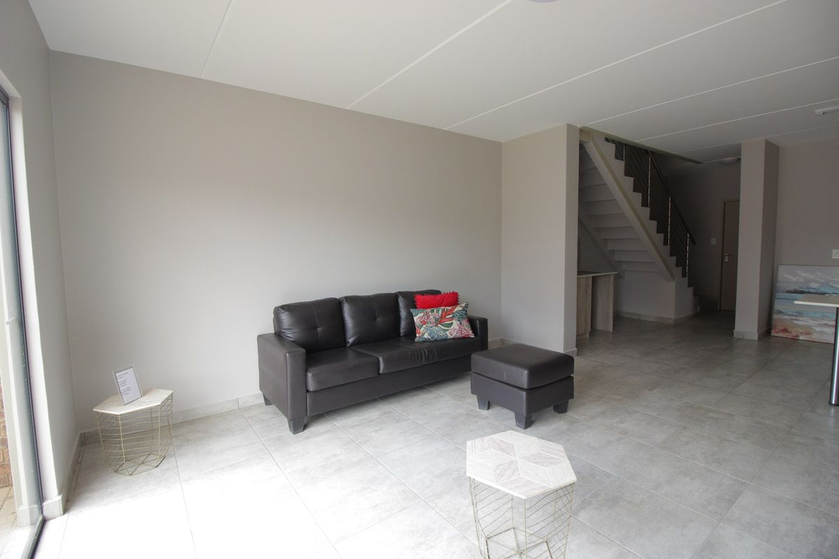 Open-plan living area featuring neutral tiled flooring, a staircase with a modern metal balustrade, and access to the exterior via a sliding glass door.